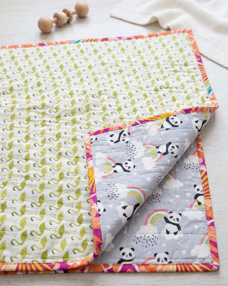 Close-up of a handmade reversible cotton baby quilt, showing the grey side with pandas and rainbows folded over the kiwi green geometric print side