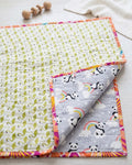 Close-up of a handmade reversible cotton baby quilt, showing the grey side with pandas and rainbows folded over the kiwi green geometric print side