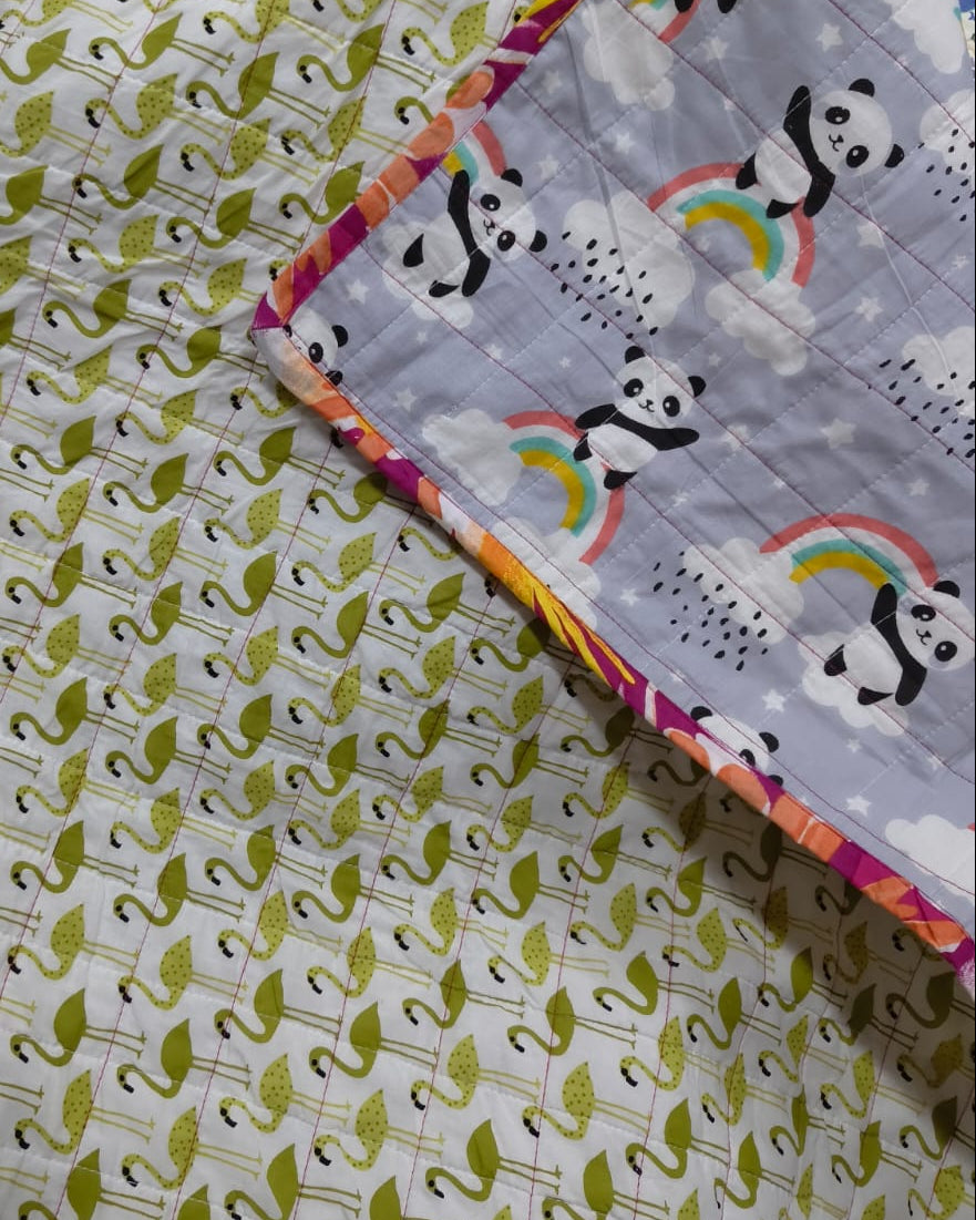 Close-up of a handmade reversible cotton baby quilt, showing the grey side with pandas and rainbows folded over the kiwi green geometric print side