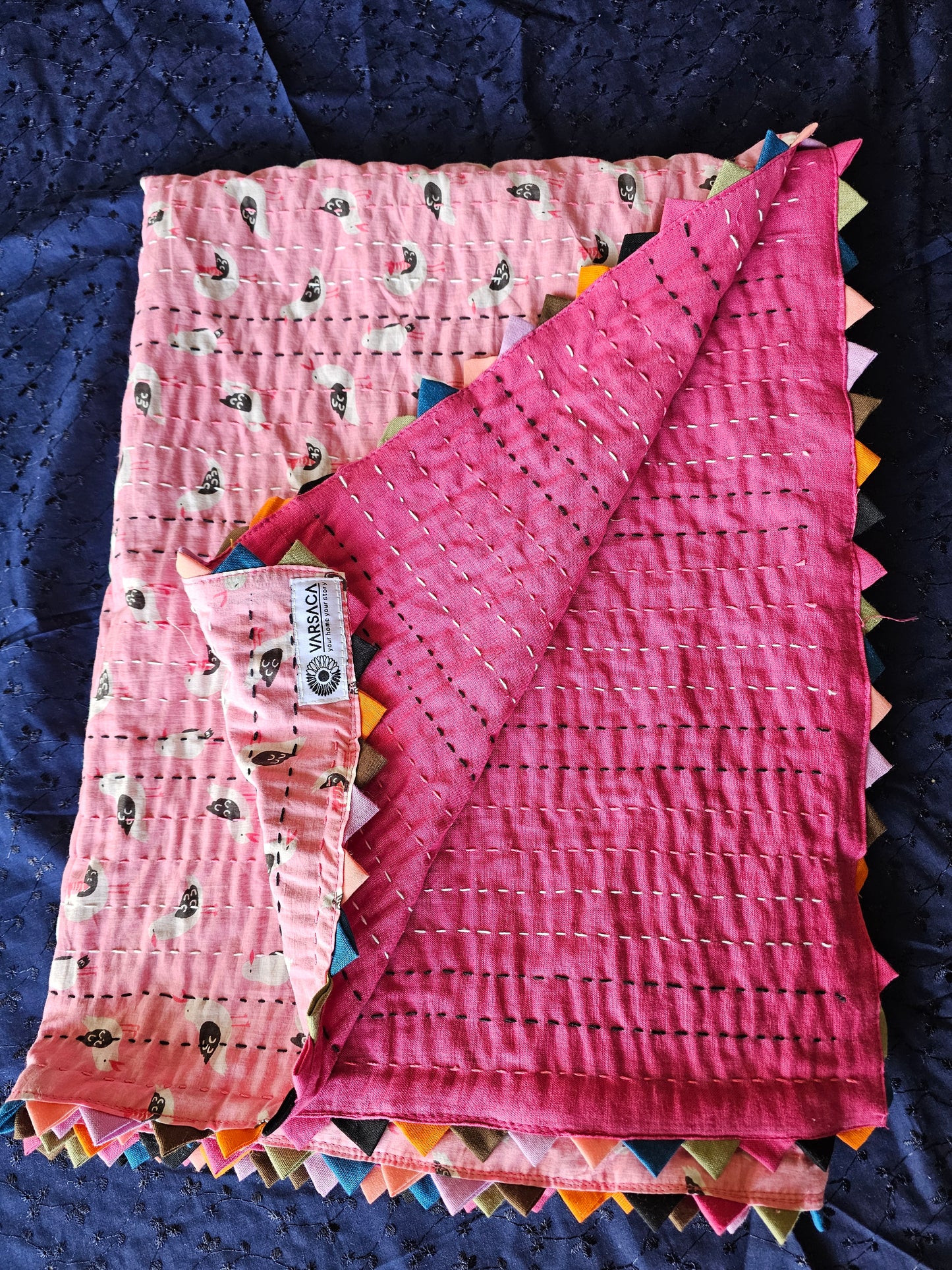 Pink quilt with colorful edges on a dark blue background