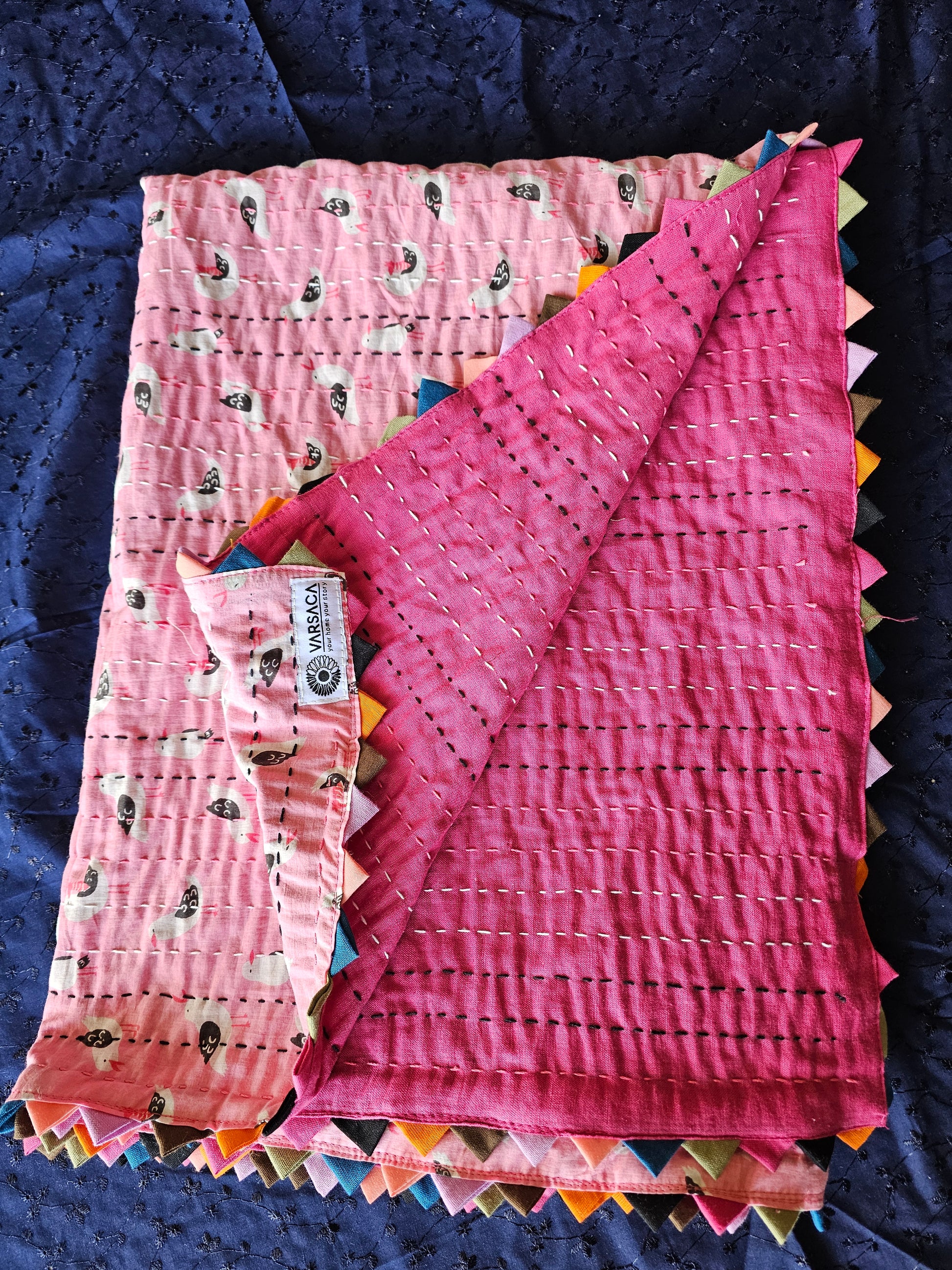 Pink quilt with colorful edges on a dark blue background