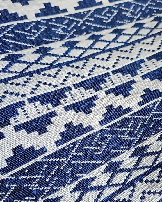 Close-up view of a royal blue and off-white woven cotton placemat featuring a detailed geometric Aztec jacquard pattern.