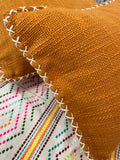 Close-up of a orange fabric with white stitching on a colorful embroidered background.