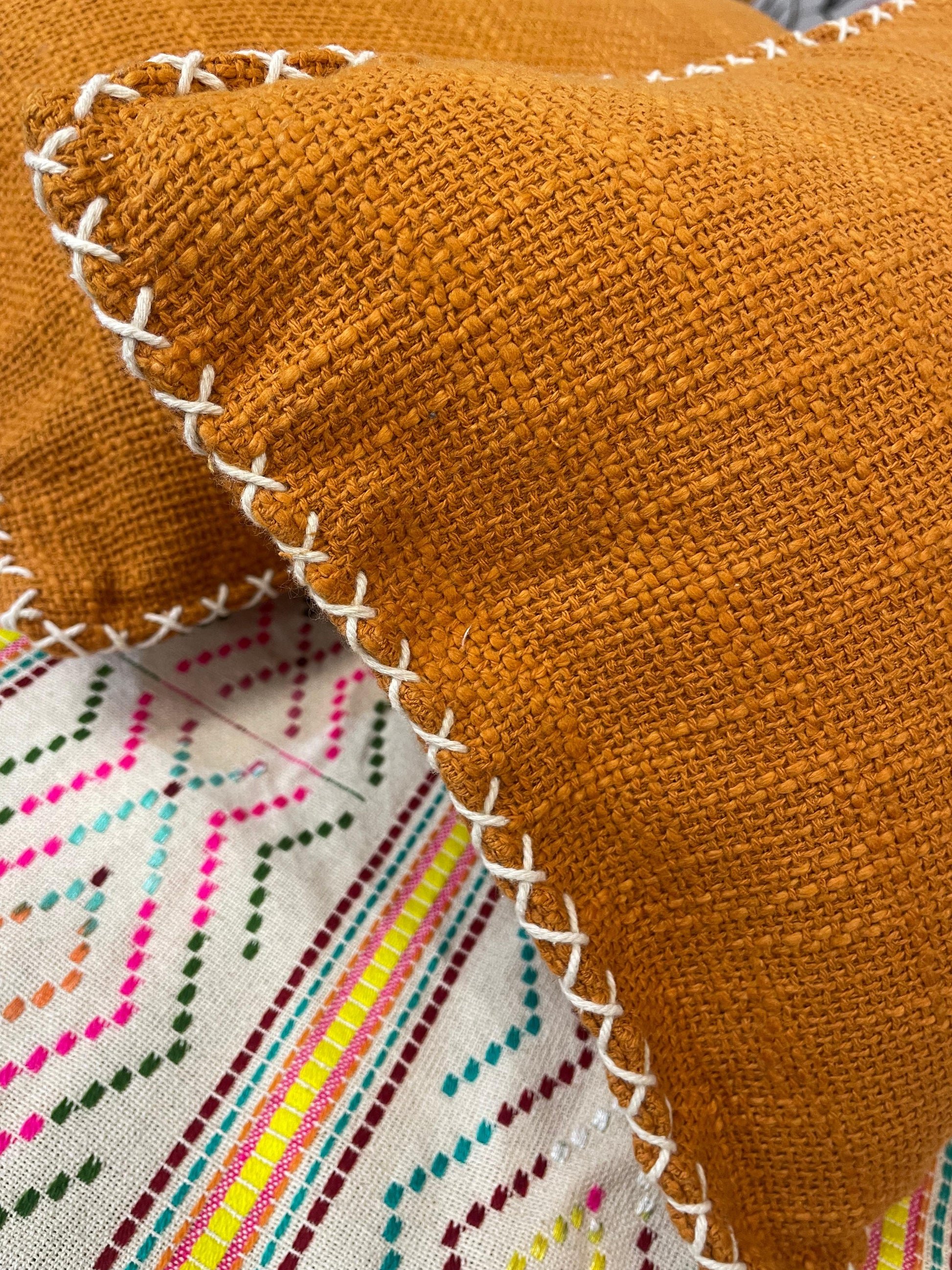 Close-up of a orange fabric with white stitching on a colorful embroidered background.