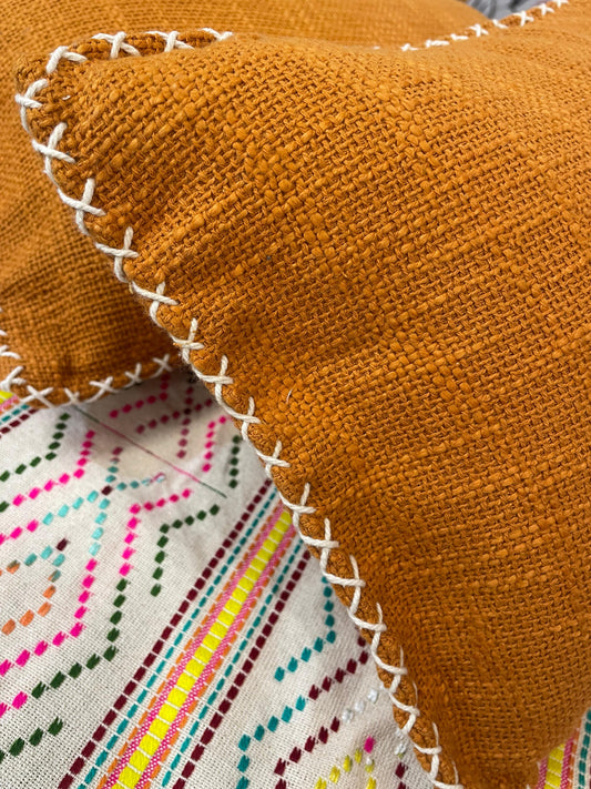 Close-up of a orange fabric with white stitching on a colorful embroidered background.