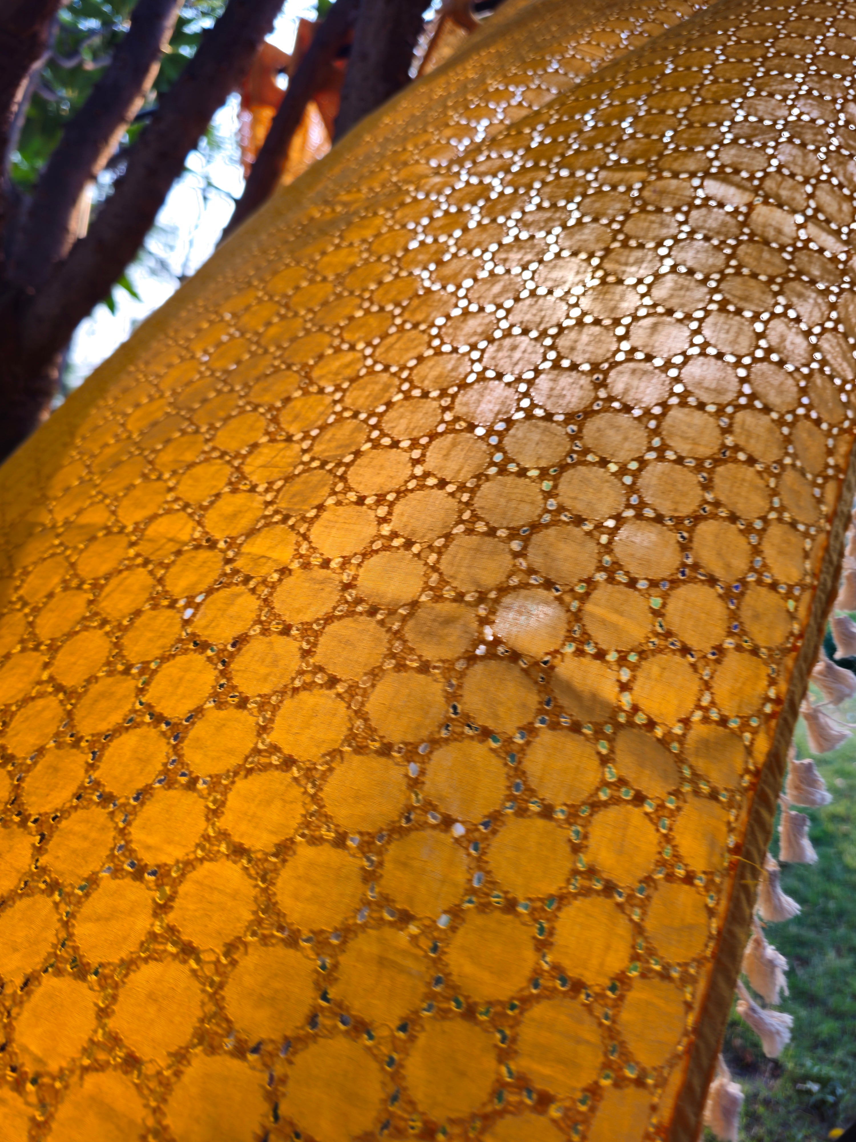 Close-up of a yellow fabric with circular patterns, possibly a dress or garment, against a blurred natural background.