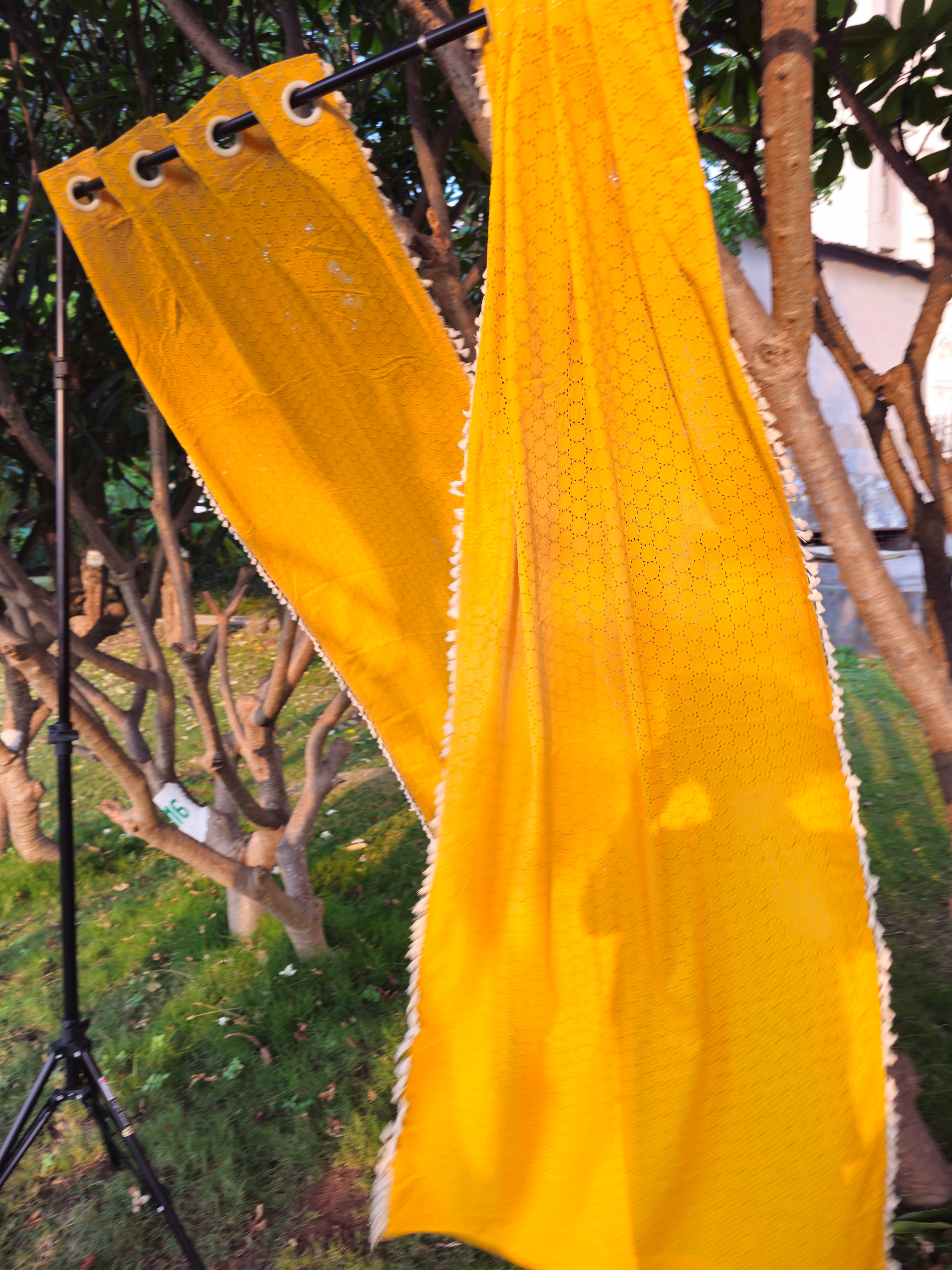 Yellow textured fabric hanging outdoors with trees and a building in the background
