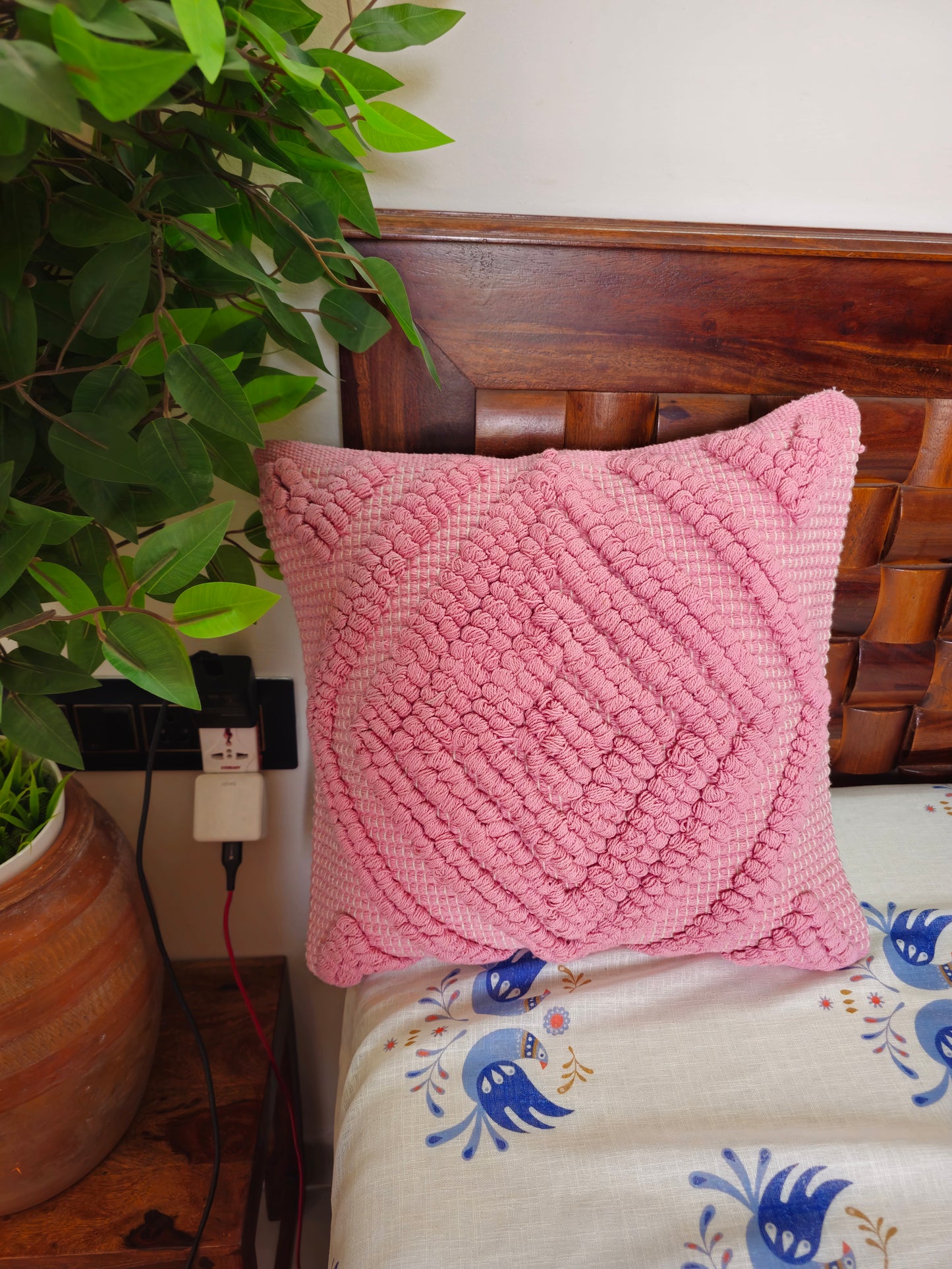 Pink textured pillow on a bed with a plant in the background