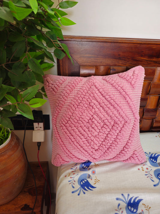Pink textured pillow on a bed with a plant in the background