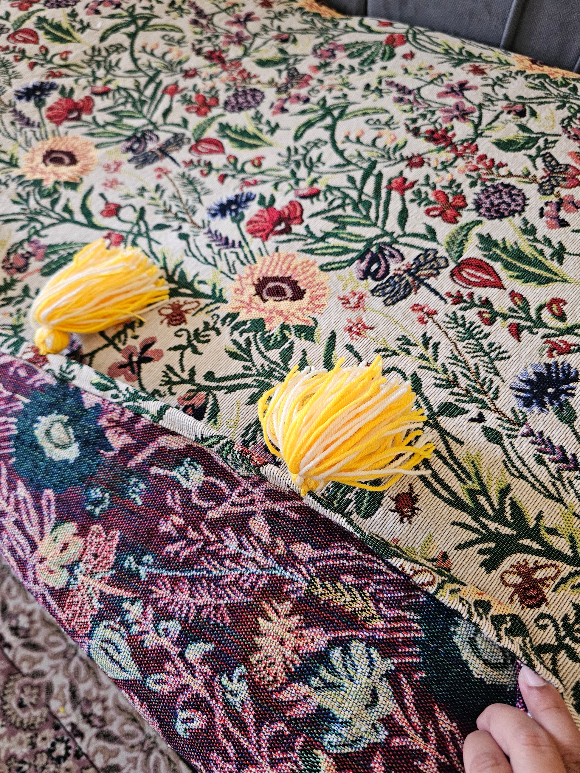 Close-up of a floral fabric with yellow tassels on a textured surface