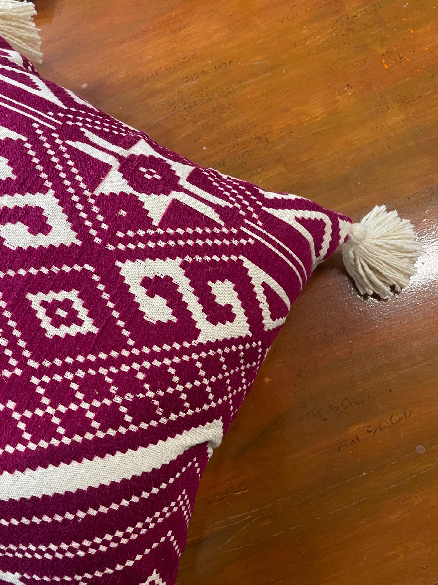Pink and white patterned pillow with tassels on a wooden surface