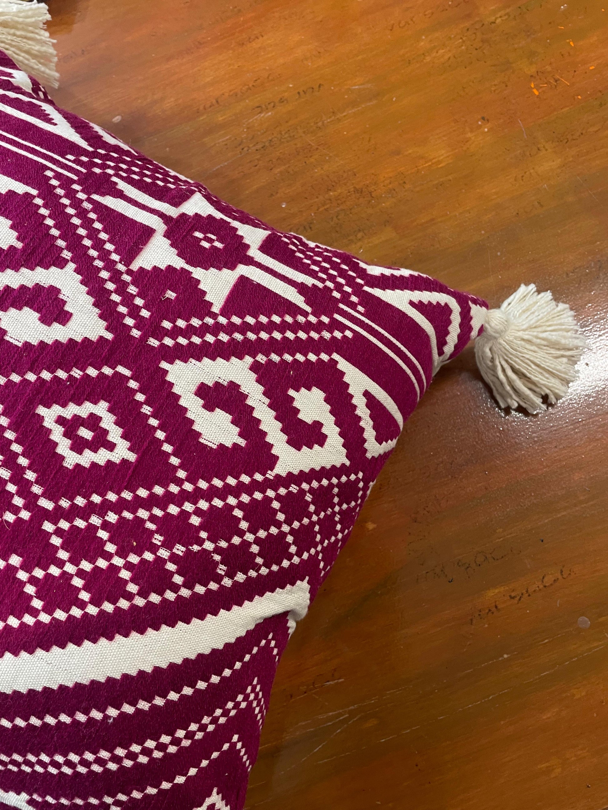 Pink and white patterned pillow with tassels on a wooden surface