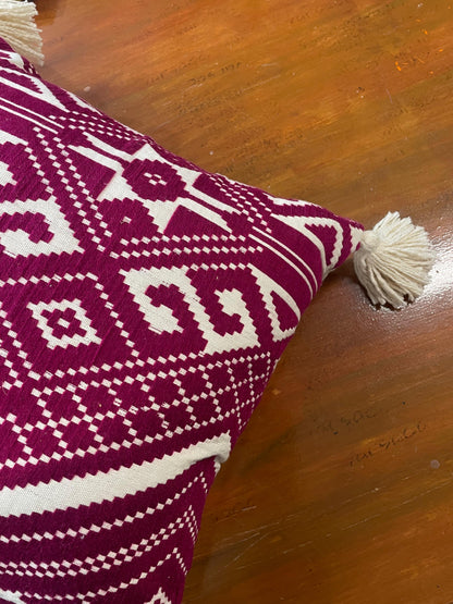 Pink and white patterned pillow with tassels on a wooden surface