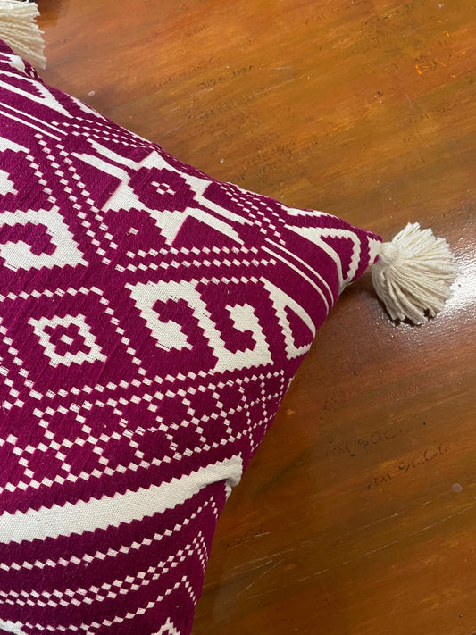 Pink and white patterned pillow with tassels on a wooden surface