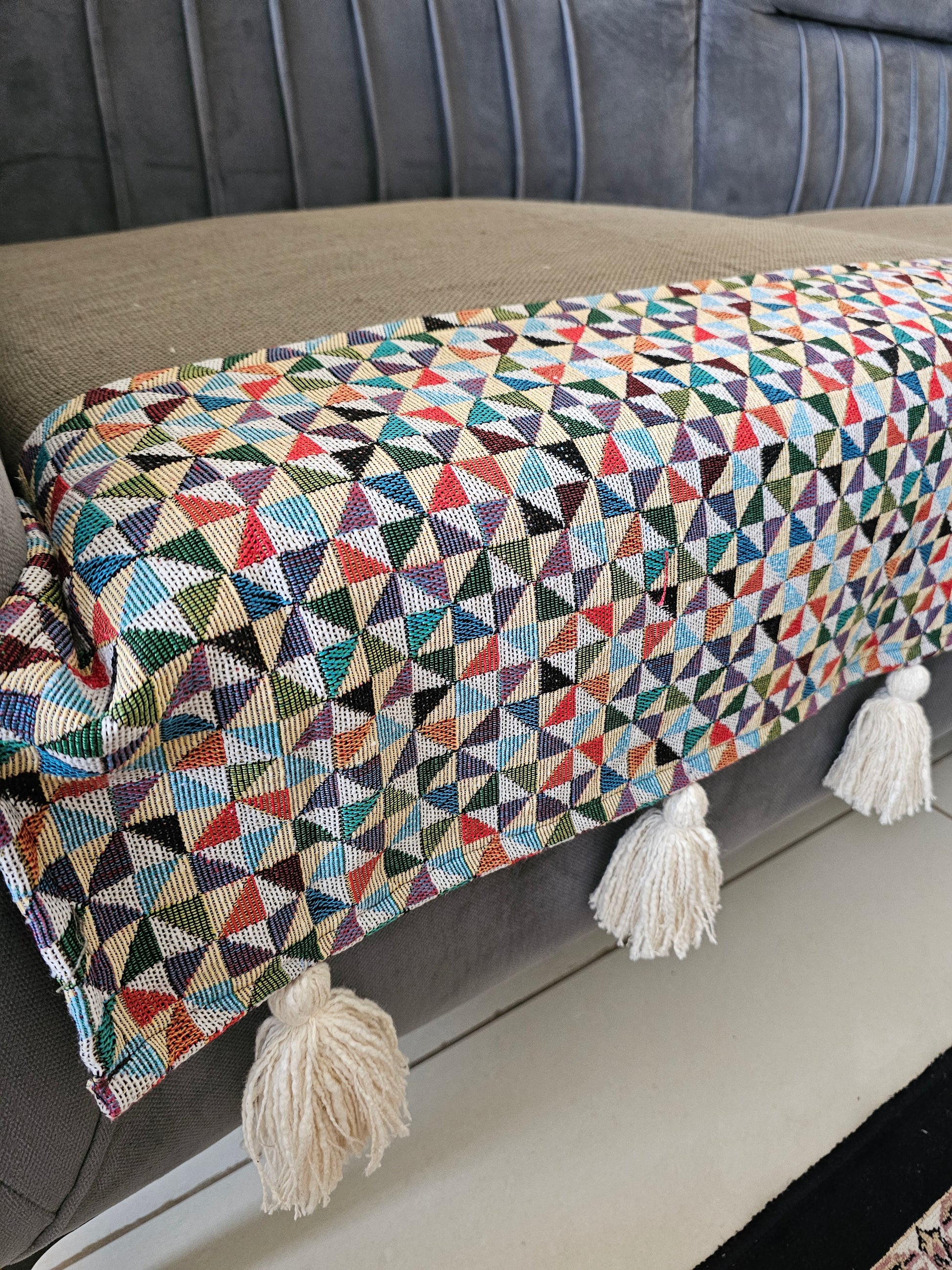 Multicolored geometric patterned throw blanket with tassels on a gray surface
