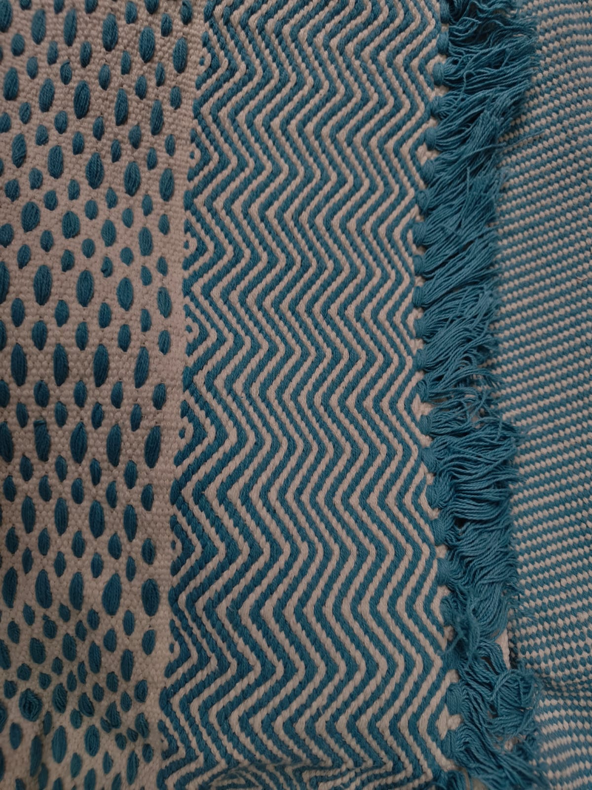 Close-up of a teal and ivory handwoven cotton tufted rug featuring textured dot patterns, geometric chevron weave, and fringe tassel edges.