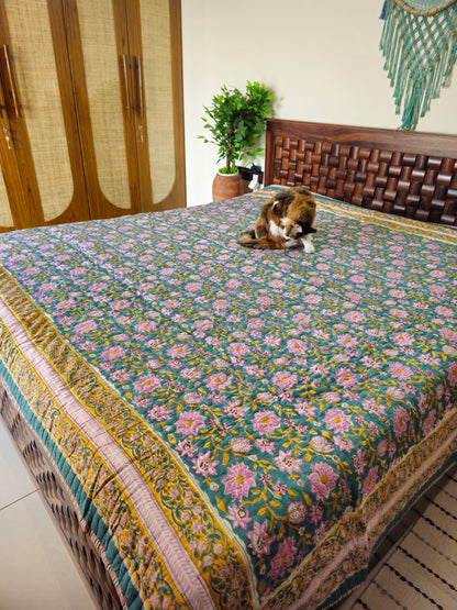 Floral patterned bedspread on a bed with a wooden headboard and a plant in the background.