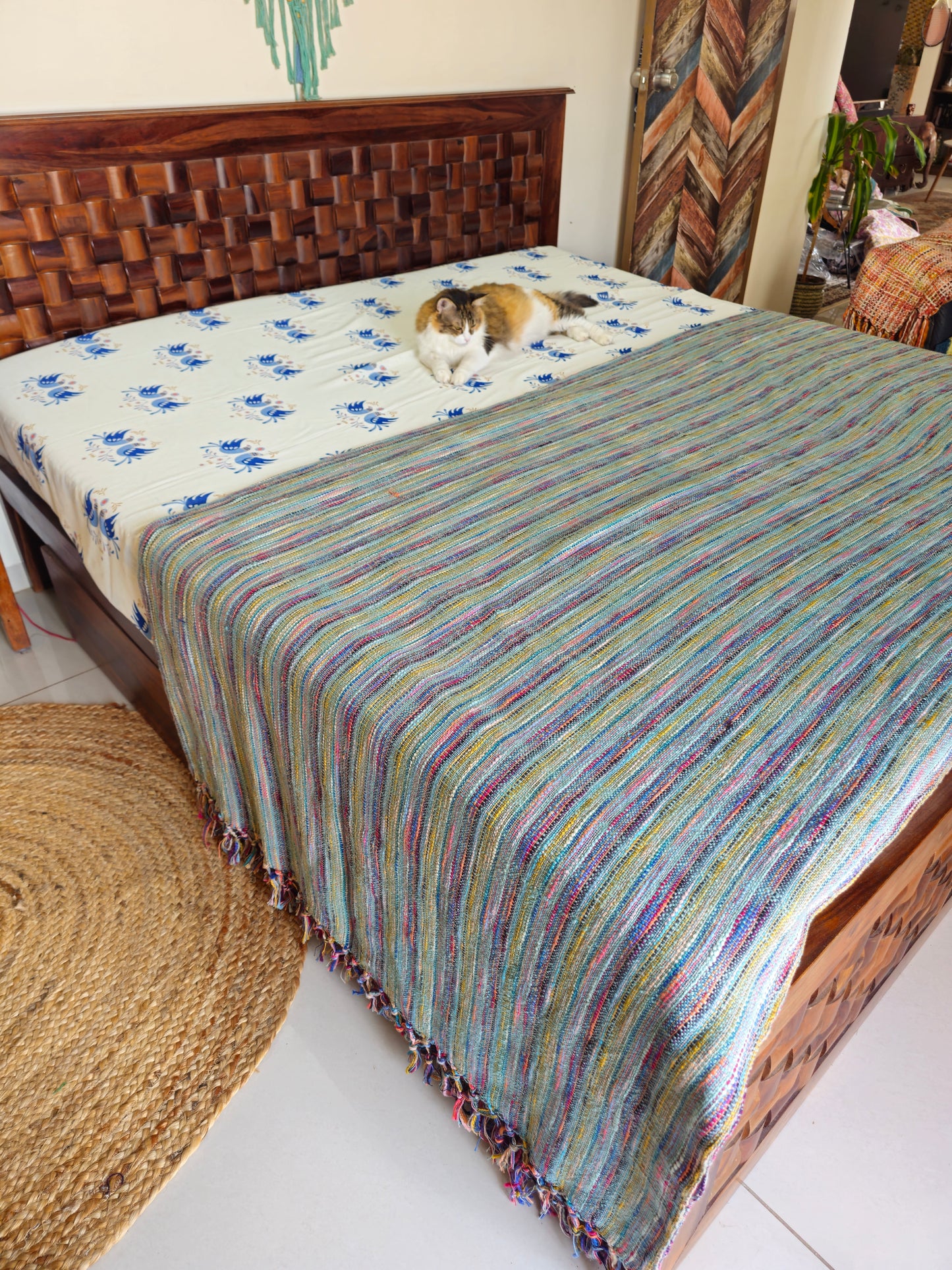Bed with a striped multicolor blanket and a cat on a white sheet.
