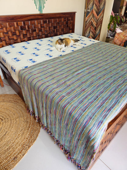 Bed with a striped multicolor blanket and a cat on a white sheet.