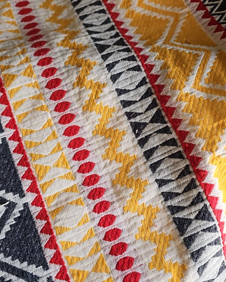 Rectangular woven cotton placemat with a mustard yellow, charcoal black, and red tribal chevron geometric pattern laid flat.