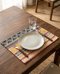 Rectangular woven cotton placemat with a mustard yellow, charcoal black, and red tribal chevron geometric pattern laid flat.
