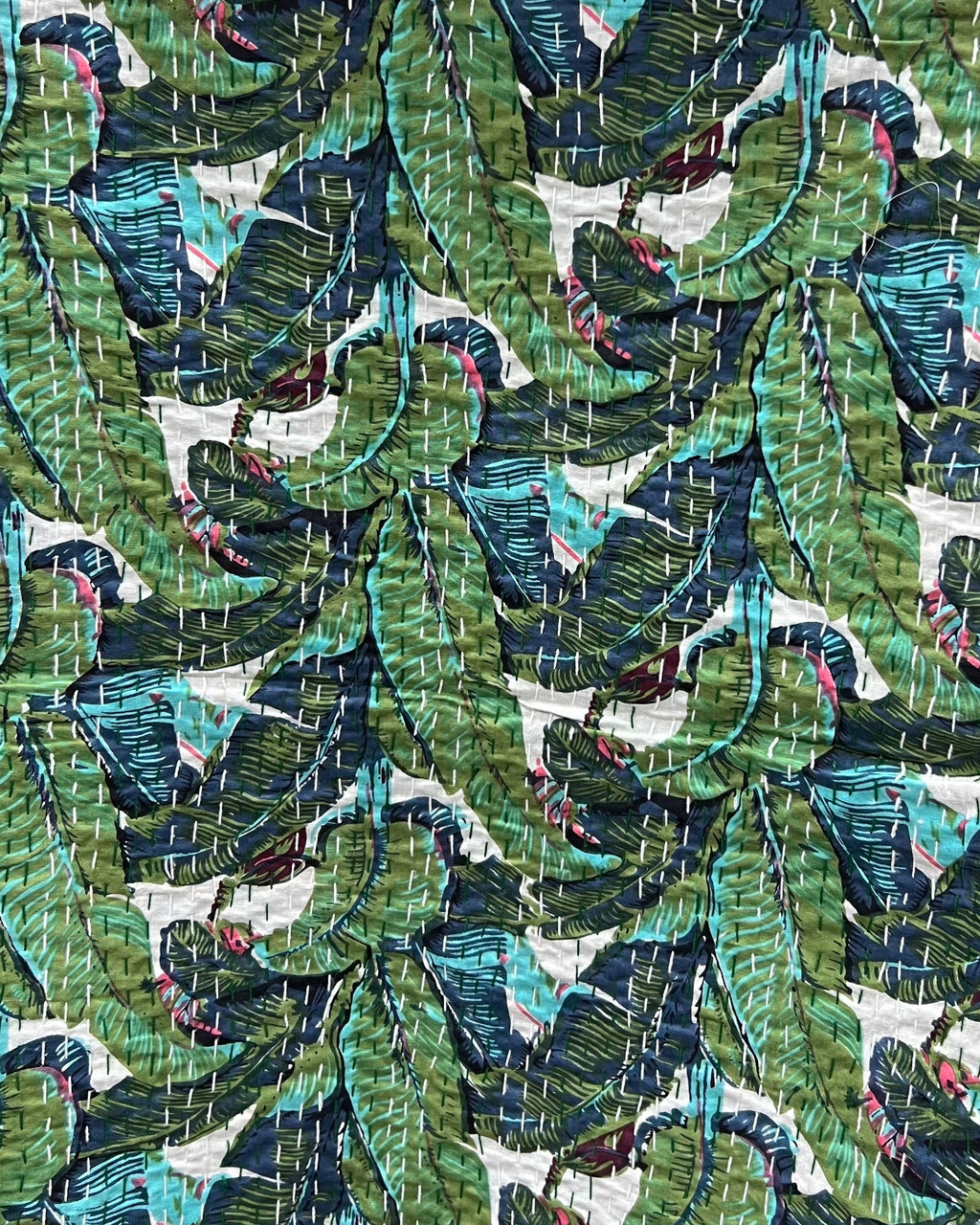 Tropical banana leaf kantha cotton quilt showcasing a vibrant botanical print on the front and a solid dark green reverse with traditional hand-stitching.