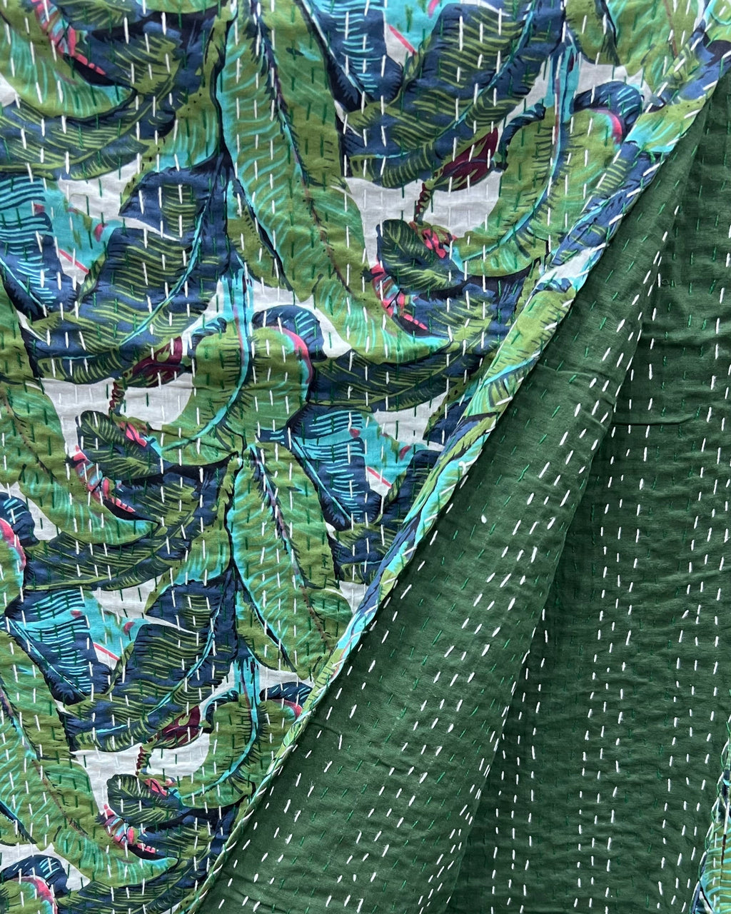 Tropical banana leaf kantha cotton quilt showcasing a vibrant botanical print on the front and a solid dark green reverse with traditional hand-stitching.