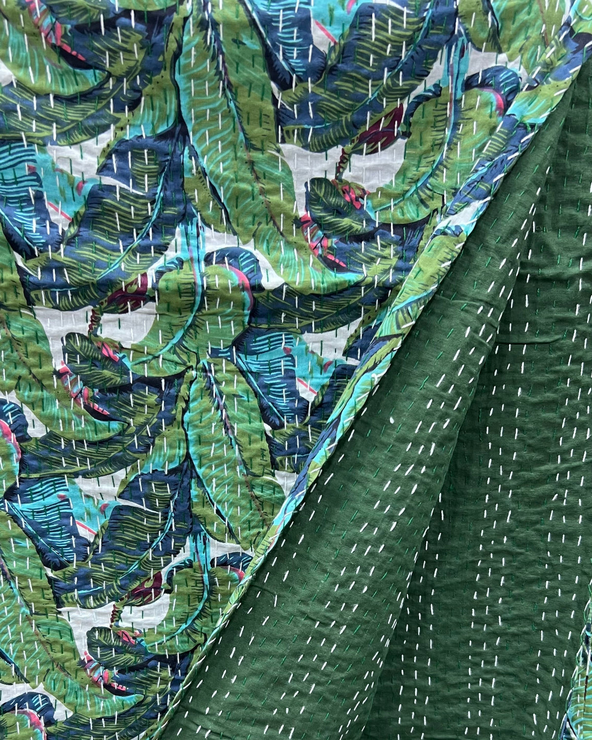 Tropical banana leaf kantha cotton quilt showcasing a vibrant botanical print on the front and a solid dark green reverse with traditional hand-stitching.