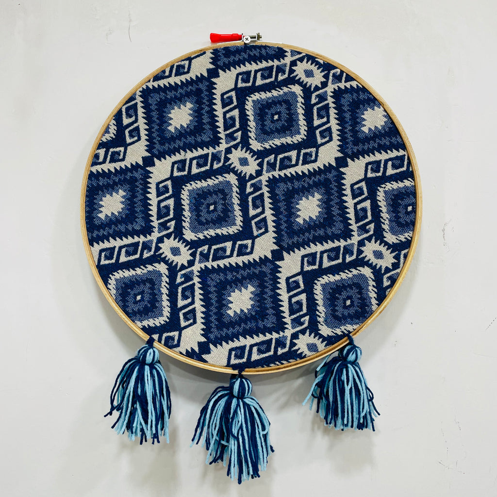 Embroidery hoop with blue and white geometric pattern and tassels on a white background