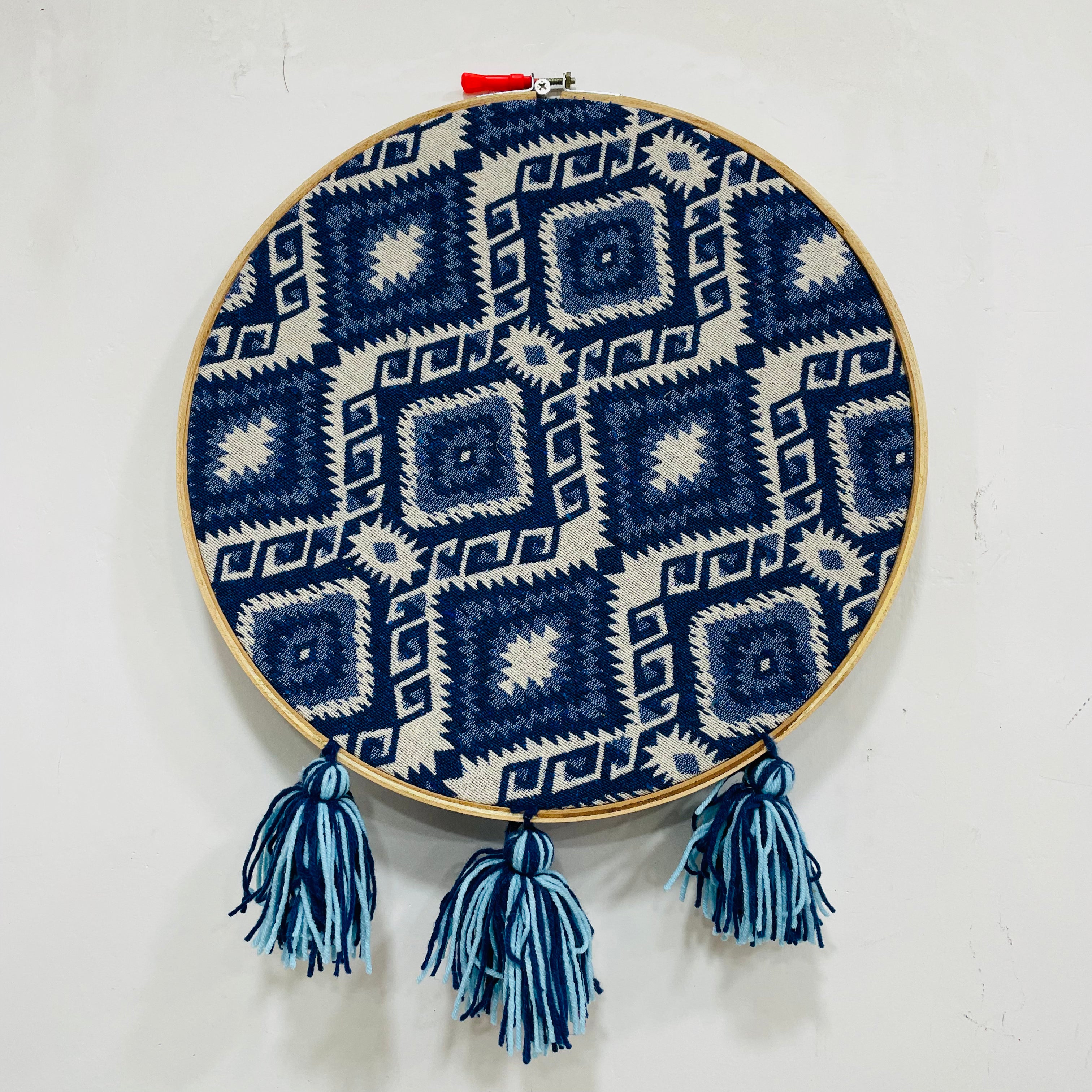 Embroidery hoop with blue and white geometric pattern and tassels on a white background