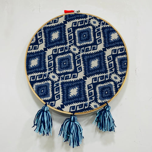 Embroidery hoop with blue and white geometric pattern and tassels on a white background