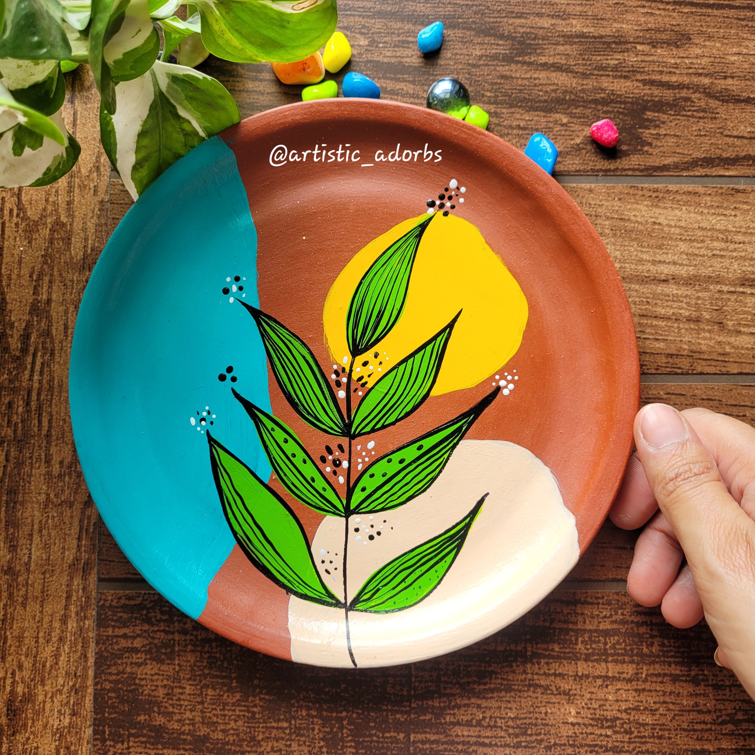 Hand-painted terracotta wall hanging plate featuring an open crescent wreath of multi-colored leaves and a wavy pastel line detail.