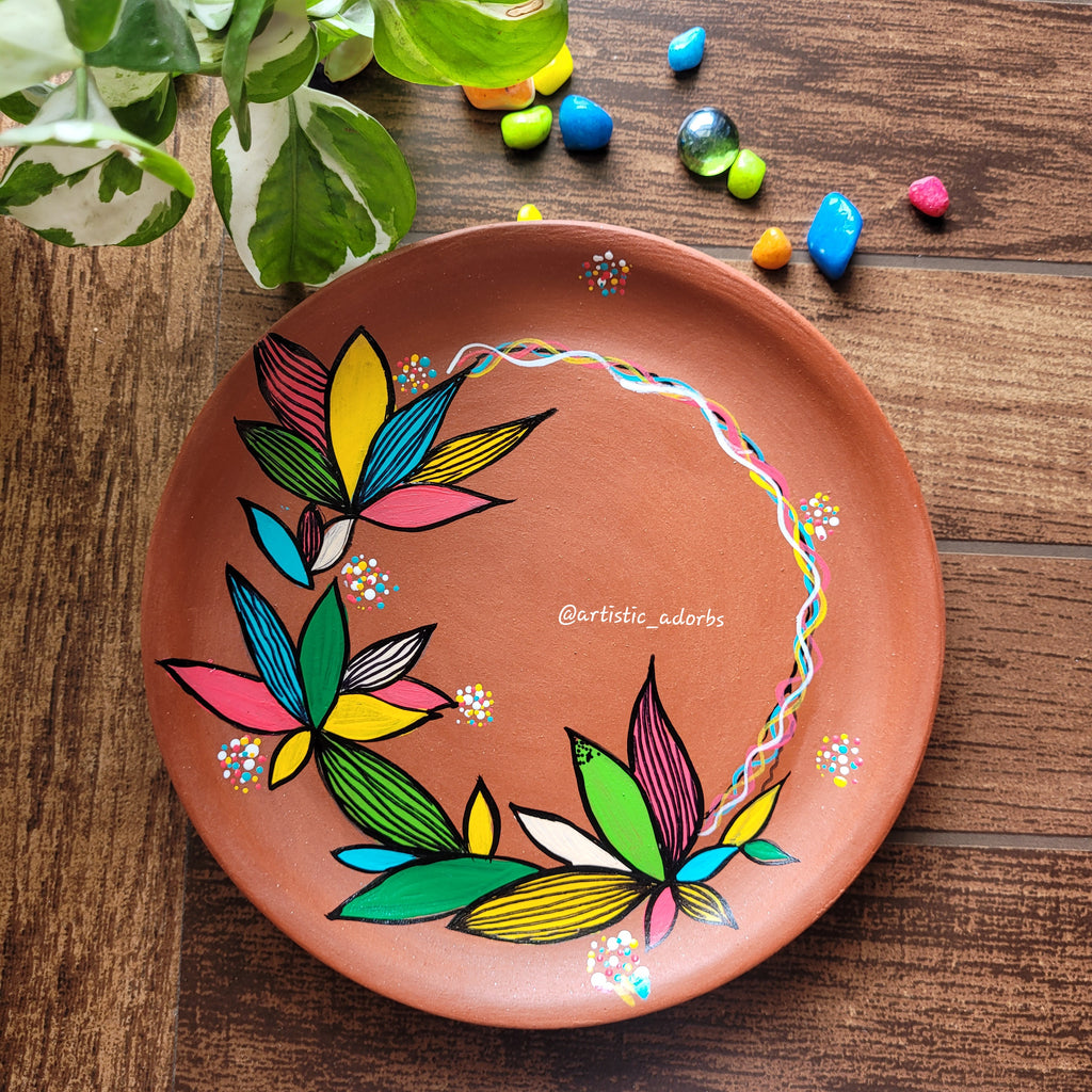 Decorative terracotta plate with colorful leaf design on a clay surface.