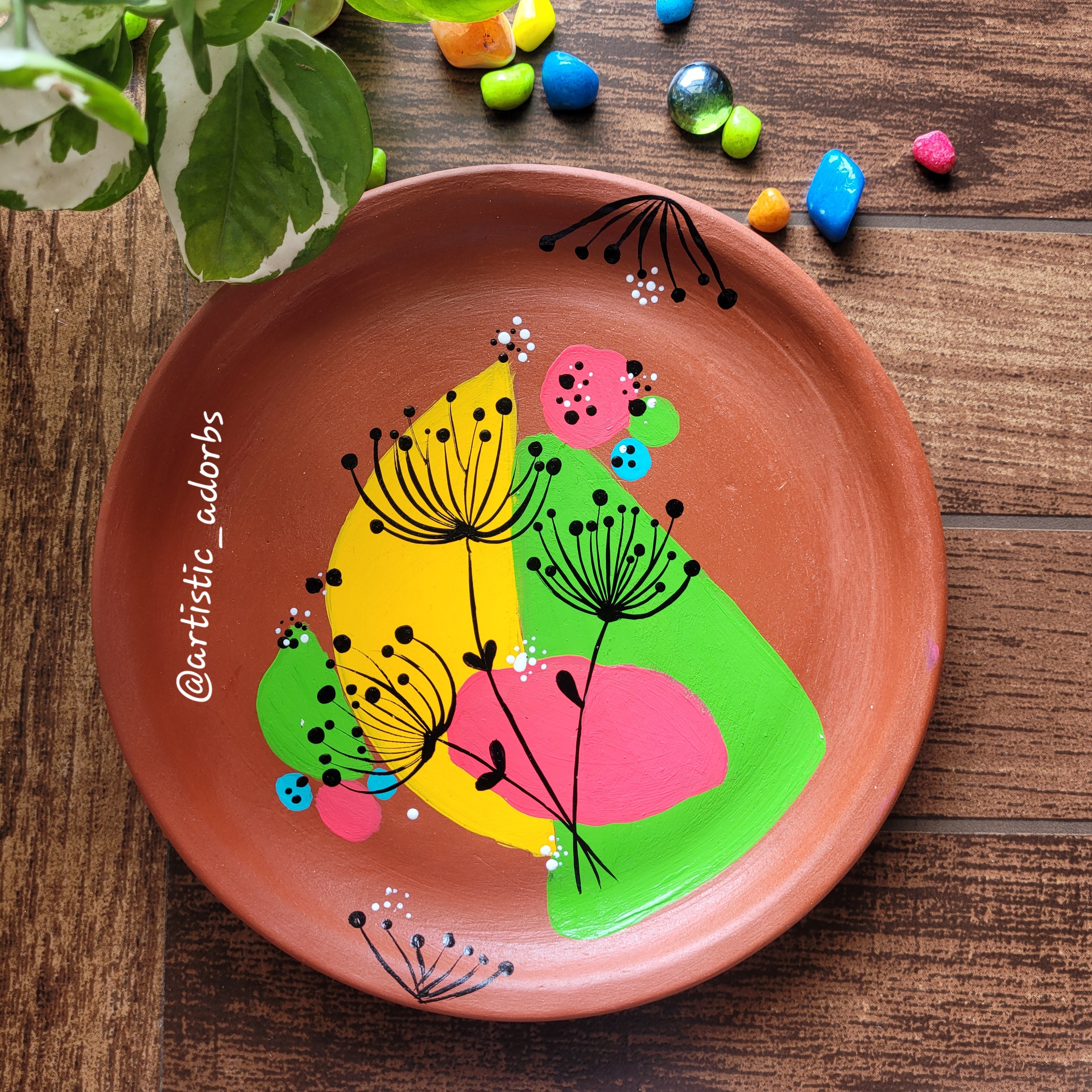 Hand-painted terracotta decorative plate featuring fine-lined black dandelion bursts over a lively, asymmetrical abstract background of lime green, bright pink, and yellow.