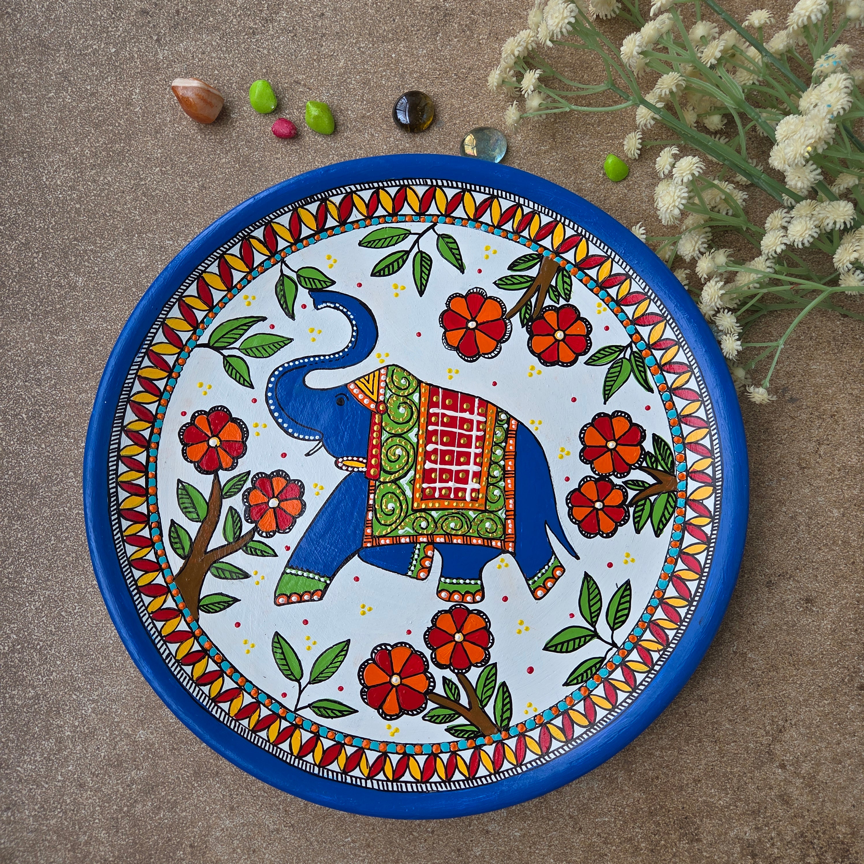 Intricate Madhubani royal elephant folk art hand-painted on an 8-inch terracotta wall plate finished with a deep blue rim.