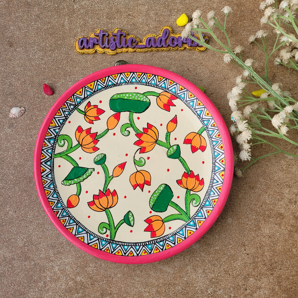Indian folk art terracotta wall plate depicting stylized Madhubani lotus stems and pods with a bright pink outer rim.