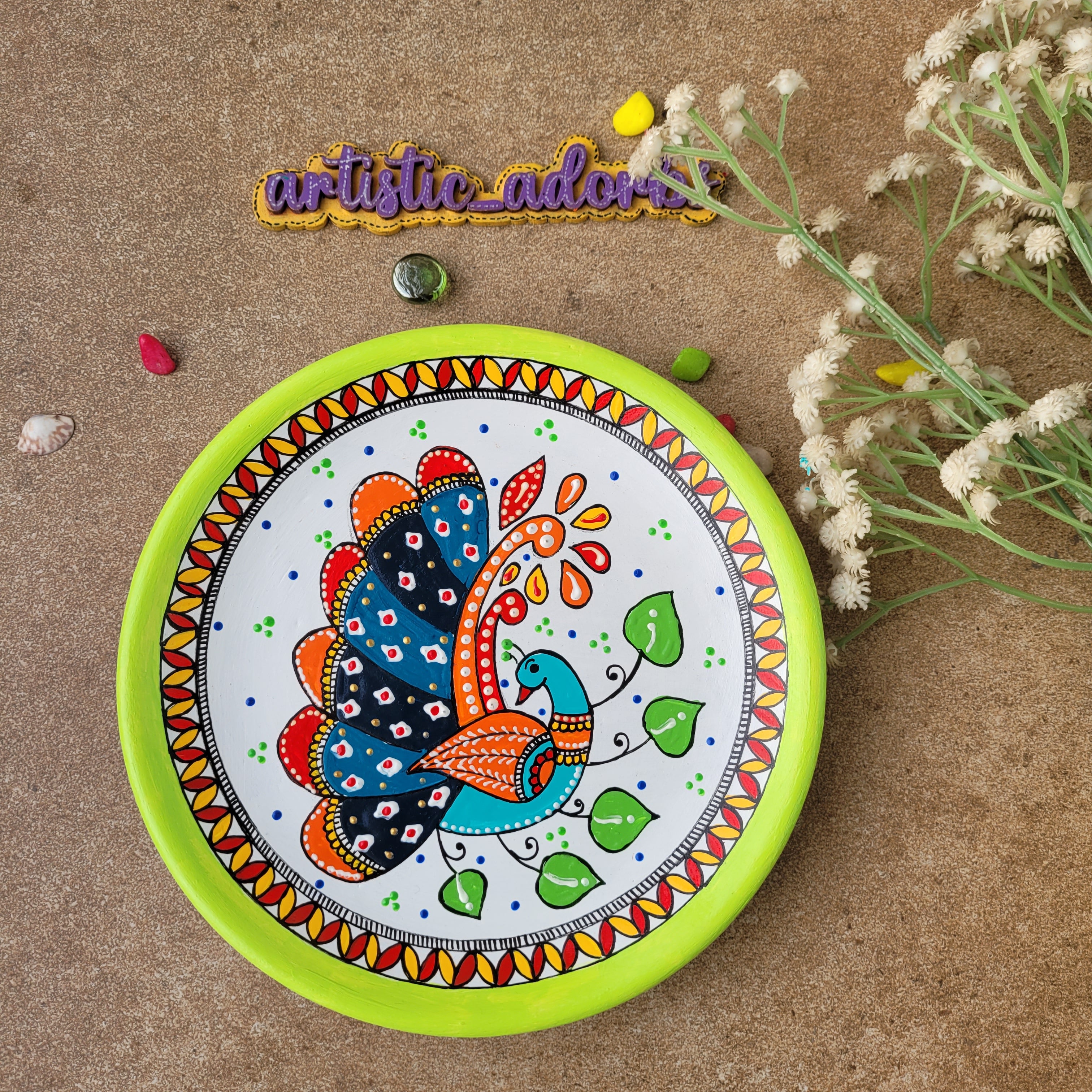Close-up of a handcrafted terracotta wall plate with a hand-painted Madhubani peacock motif, intricate line work, and a lime green border.