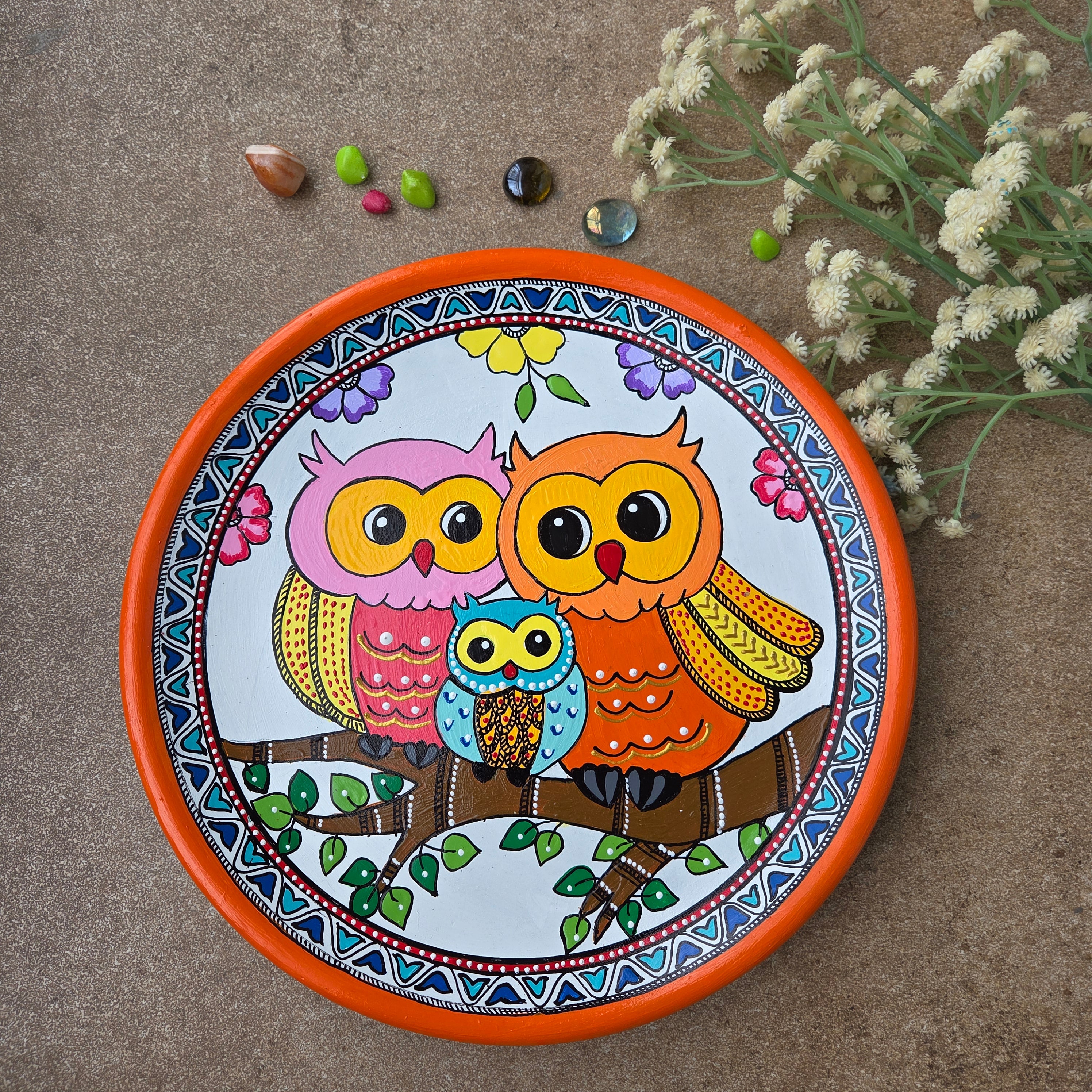 Traditional Madhubani hand-painted clay plate featuring a family of three decorative owls perched on a branch with an orange border.