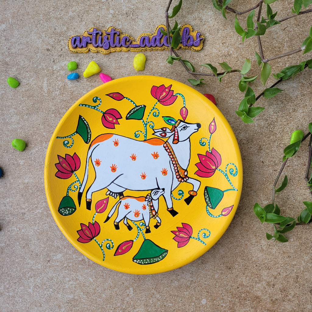 Handcrafted 8-inch terracotta plate featuring a hand-painted Pichwai cow and calf motif on a bright yellow background.