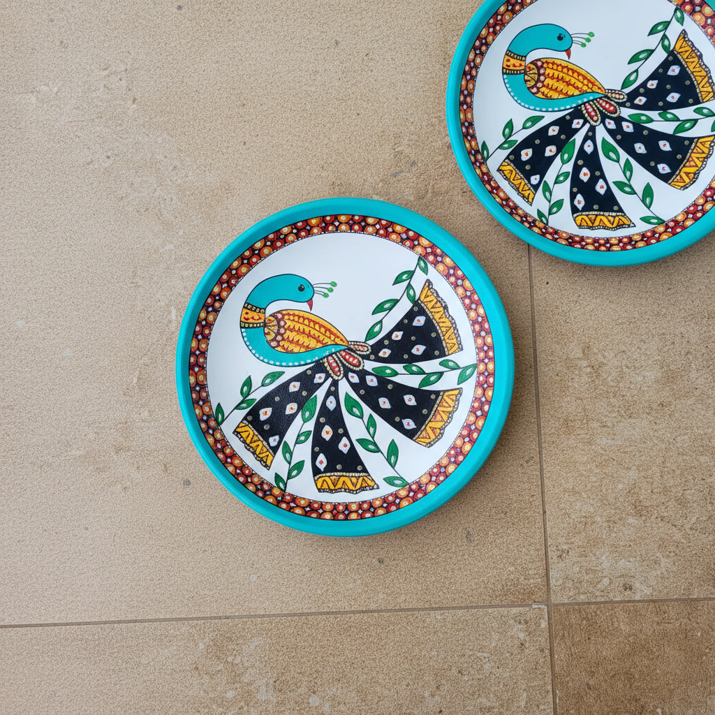 White circular terracotta plate hand-painted with a detailed blue and black Pichwai style peacock motif.