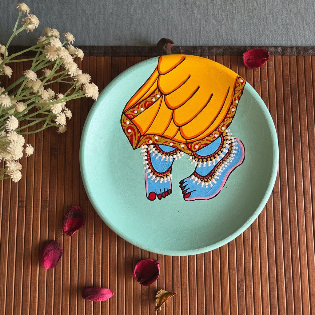 Traditional Pichwai terracotta wall art displaying Shrinathji's blue feet and yellow dhoti over a pastel mint-green background.