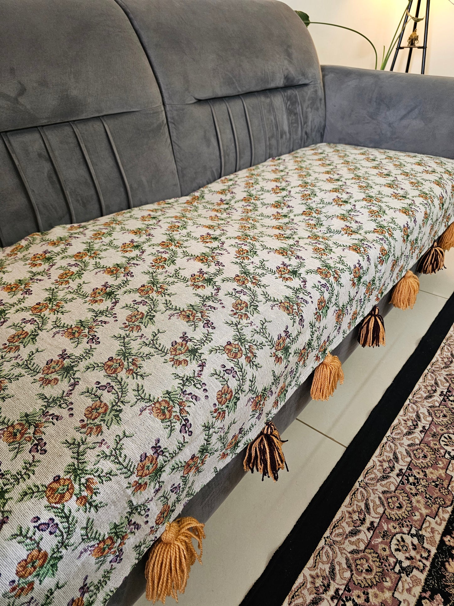 Floral-patterned throw blanket with tassels on a gray sofa