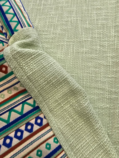 Close-up of a green textured fabric with a colorful patterned fabric underneath