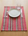 Rectangular handwoven cotton table placemat featuring horizontal hot pink, orange, green, and cream striped geometric patterns laid flat.