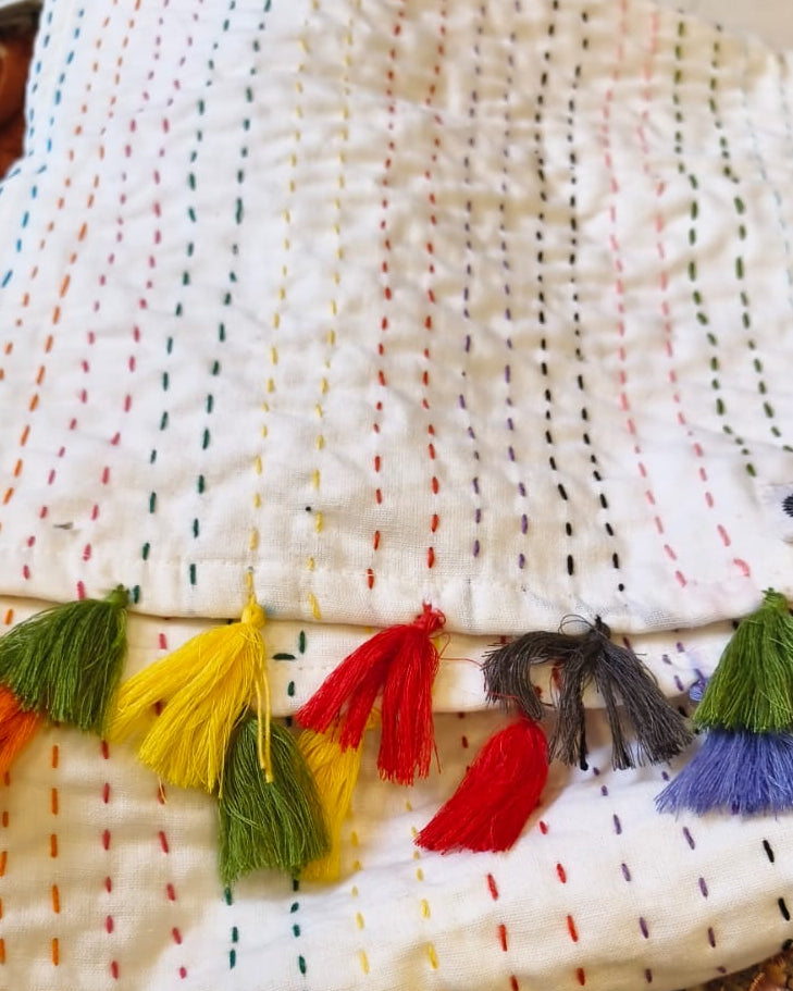 White cotton dining table runner featuring multicolored vertical running stitches and a colorful arrangement of yarn tassels along the edge, with Vasaca brand labels.