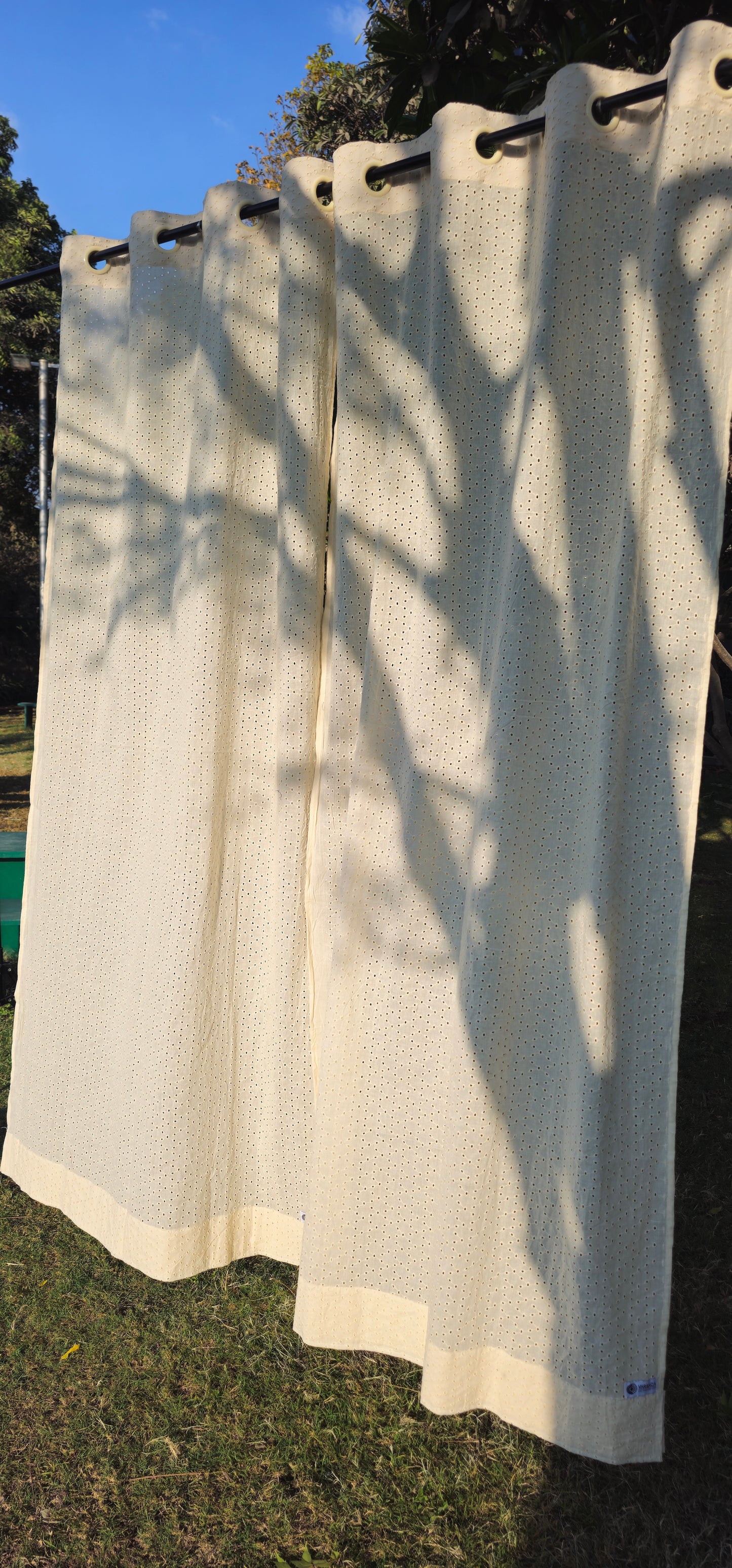Beige outdoor curtains with grommets on a rod against a natural background.