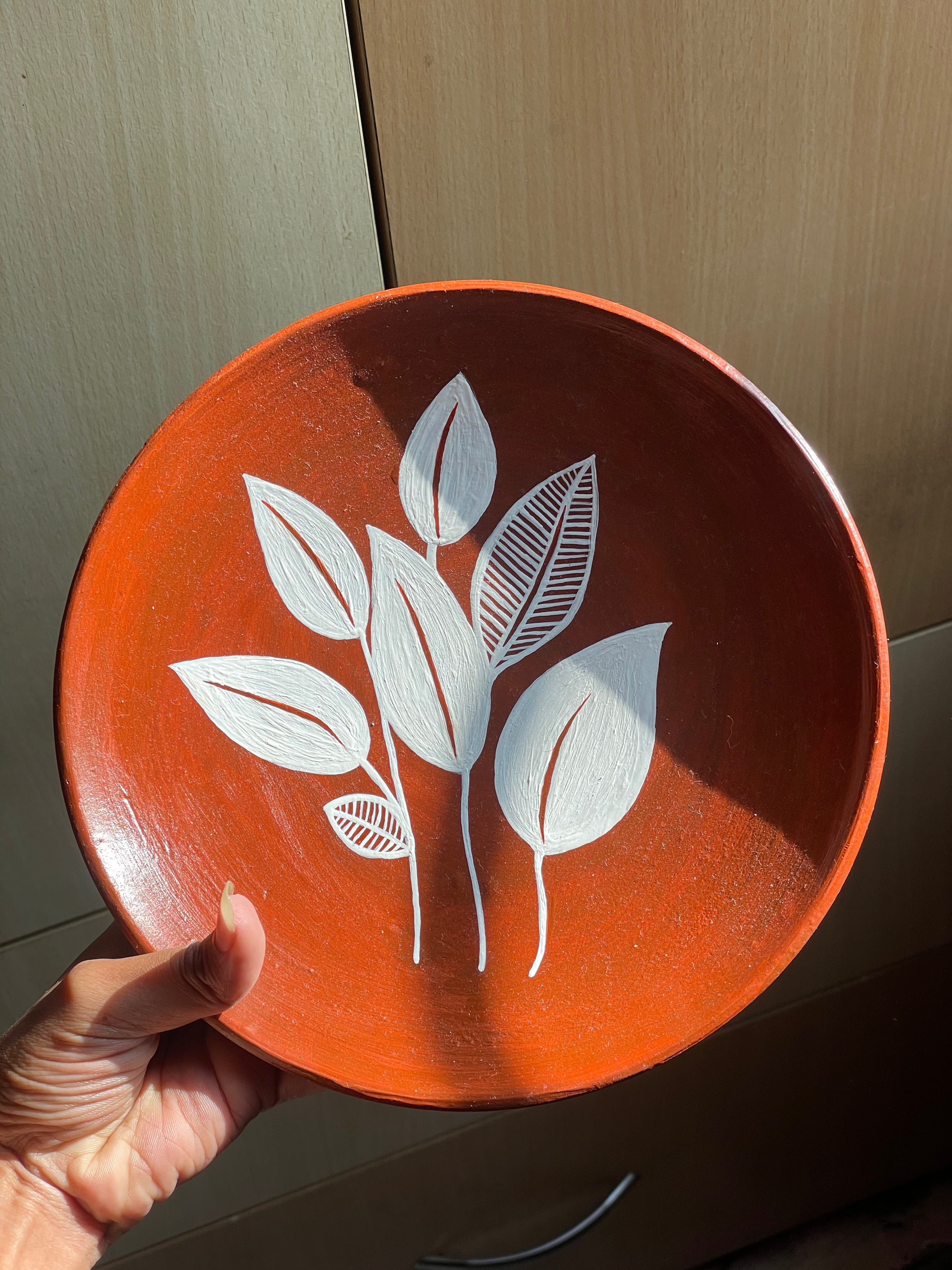 Hand holding a red plate with white leaf design against a wooden background