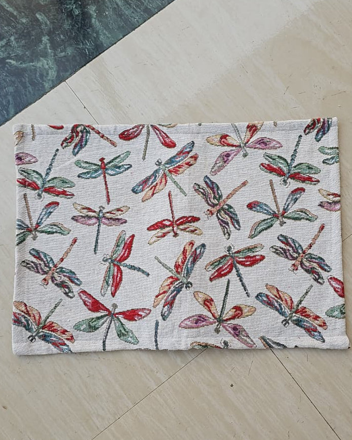 Rectangular woven cotton table placemat with a colorful red, green, and yellow dragonfly motif on an off-white cream background.