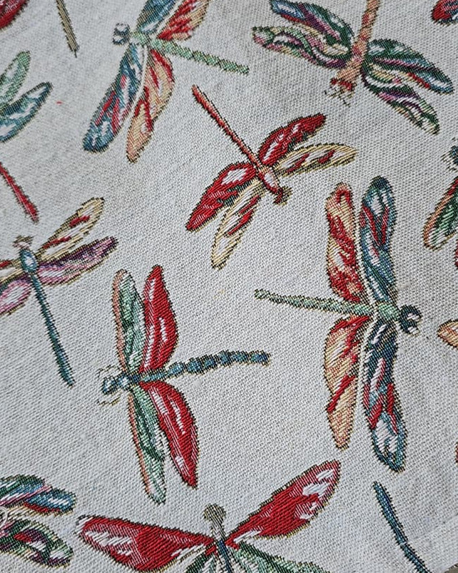 Rectangular woven cotton table placemat with a colorful red, green, and yellow dragonfly motif on an off-white cream background.