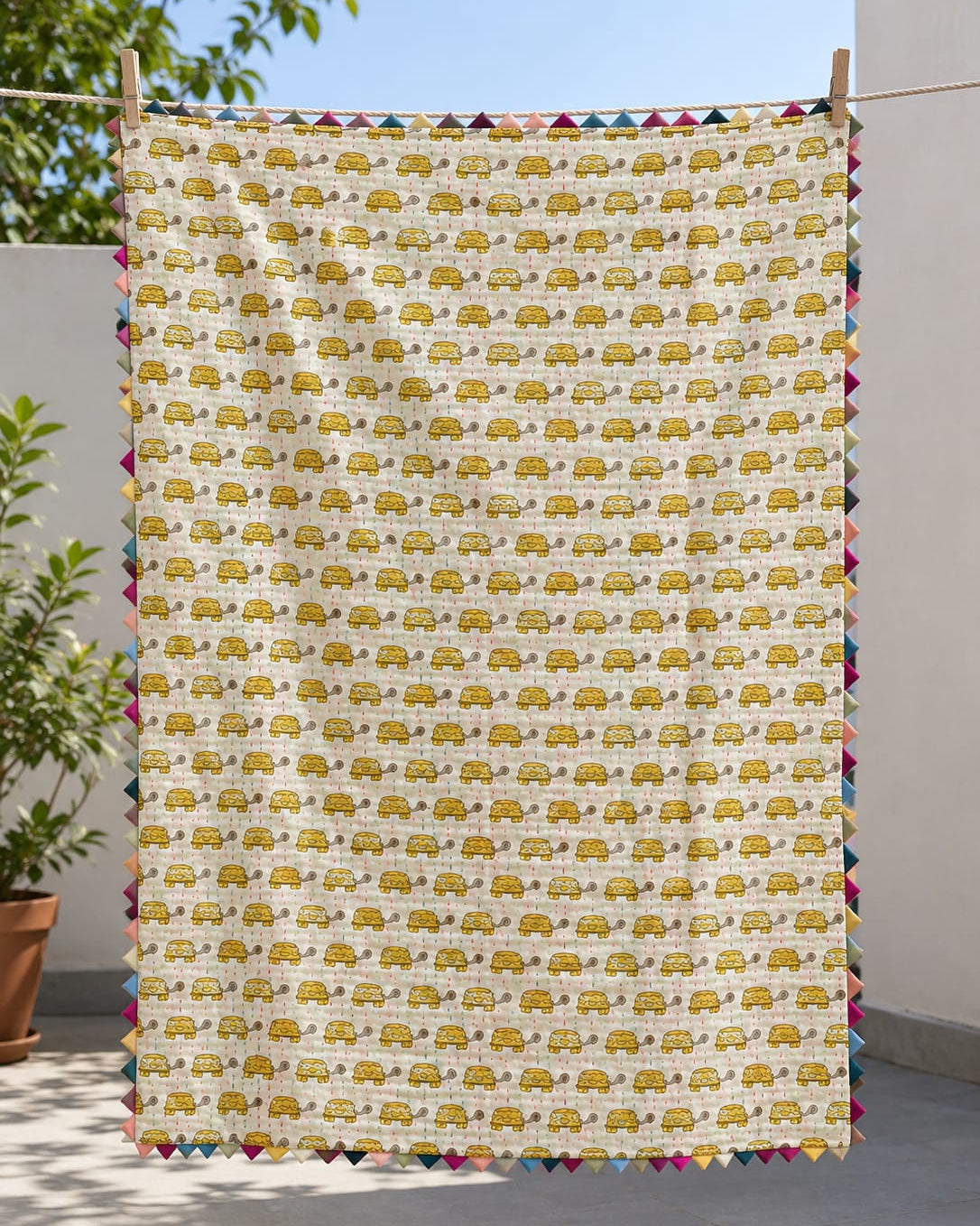 Close-up of a handmade reversible Kantha cotton baby quilt showing the solid neutral reverse side with multi-colored hand stitching folded over the yellow turtle print and colorful triangle edge binding.